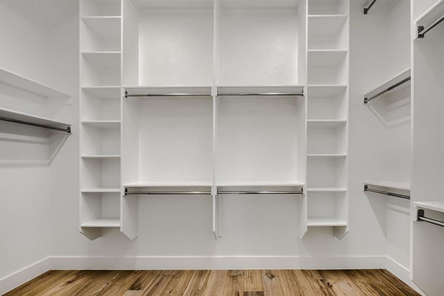 Spacious closet featuring white built-in shelving, chrome hanging rods, and wood-finish flooring