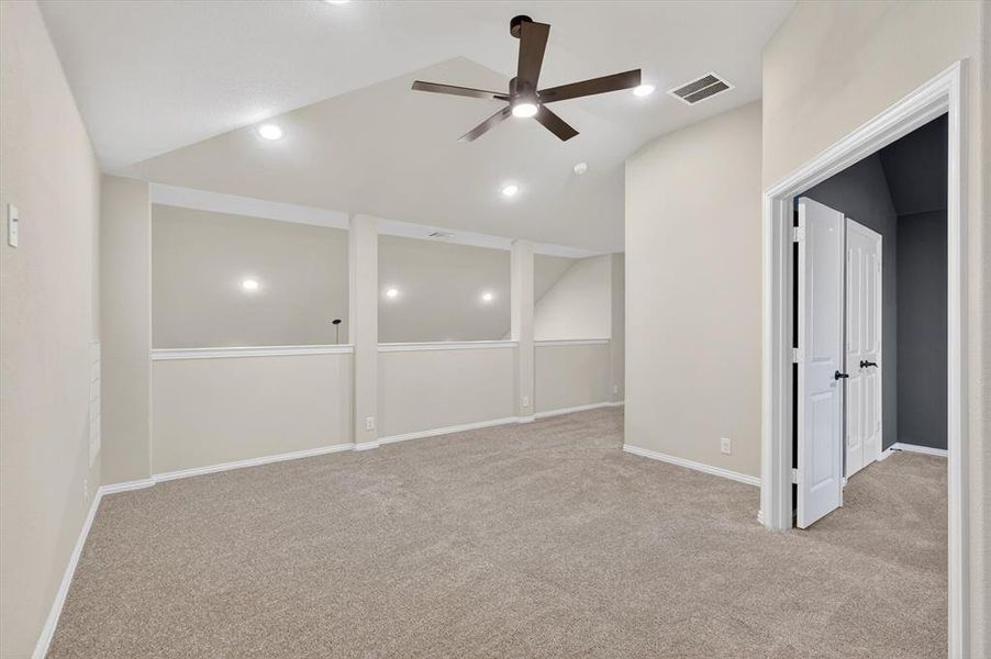 Versatile open loft space featuring vaulted ceilings, recessed lighting, a contemporary ceiling fan, plush carpet flooring, and white trim molding Versatile open loft space featuring vaulted ceilings, recessed lighting, a contemporary ceiling fan, plush carpet flooring, and white trim molding