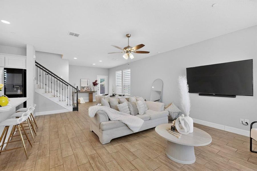 This open-concept living area features wood-look tile flooring, light grey walls, and a ceiling fan