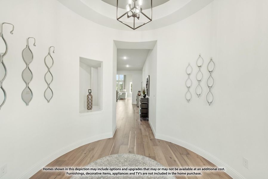 Rounded foyer with hardwood floors, geometric chandelier, wall niches, and hallway leading to living area