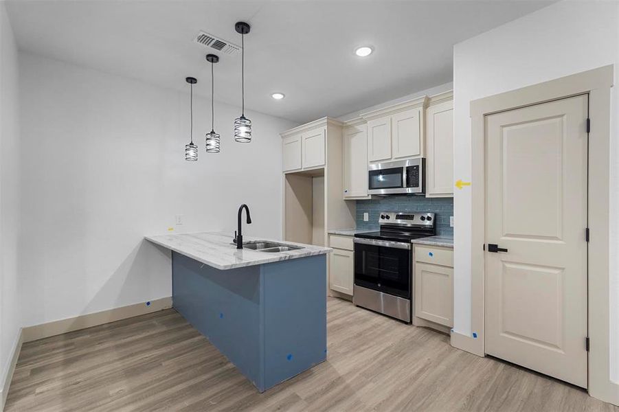 Kitchen with light wood finished floors, a peninsula, a sink, decorative backsplash, and appliances with stainless steel finishes