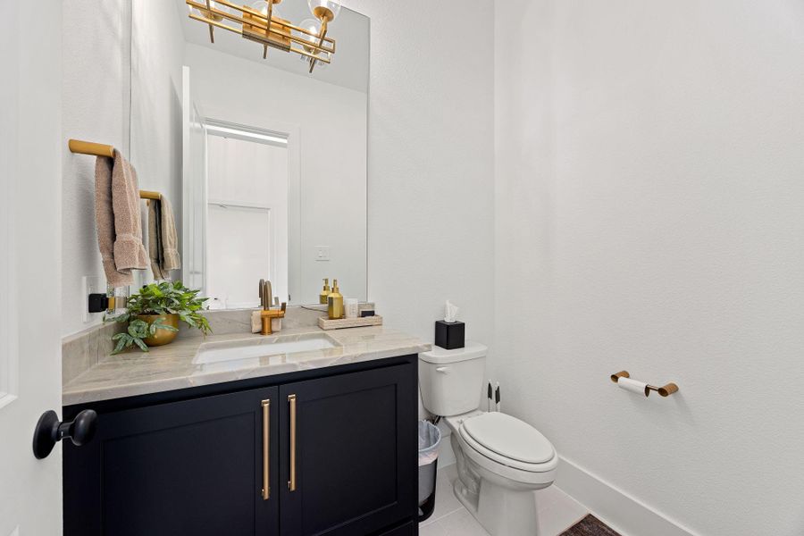 A beautiful half bathroom with a sleek design. It features a black vanity with gold accents and a large mirror
