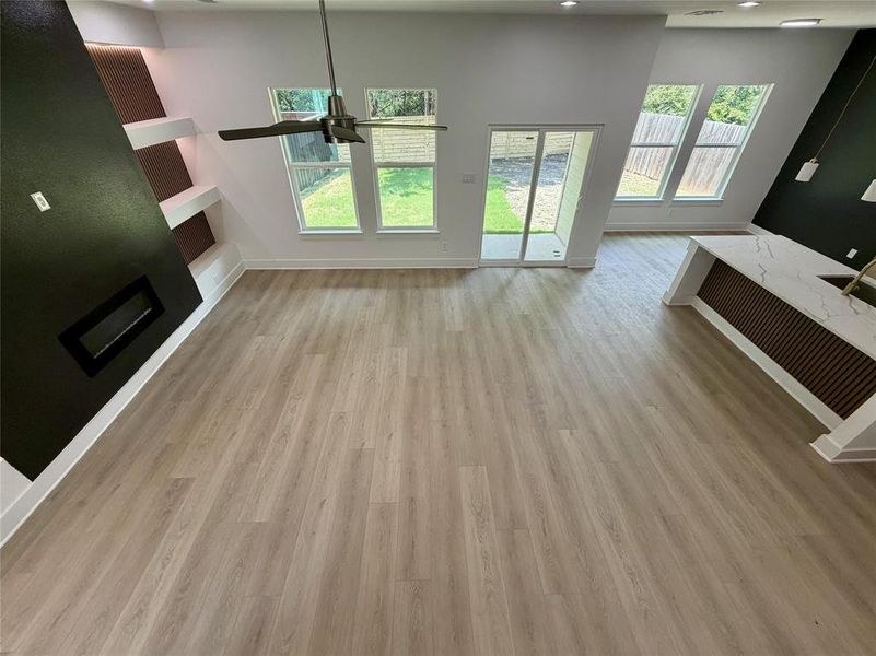 Spacious open-concept living area featuring light wood-finish flooring, a modern fireplace with a black surround, and built-in shelving Spacious open-concept living area featuring light wood-finish flooring, a modern fireplace with a black surround, and built-in shelving