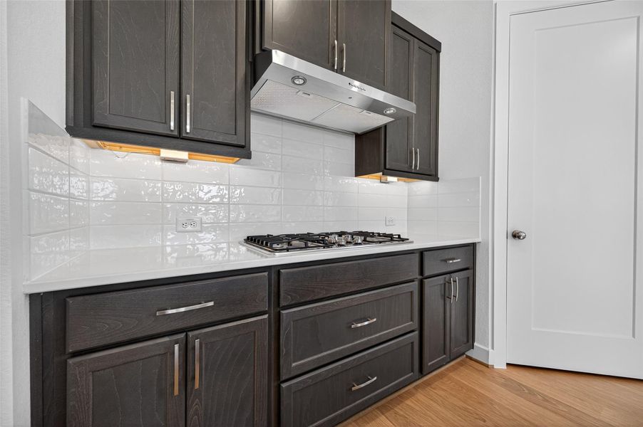 This kitchen showcases a sleek gas cooktop with stylish dark cabinetry and a glossy backsplash. The modern design and under-cabinet lighting add both beauty and functionality to the space.