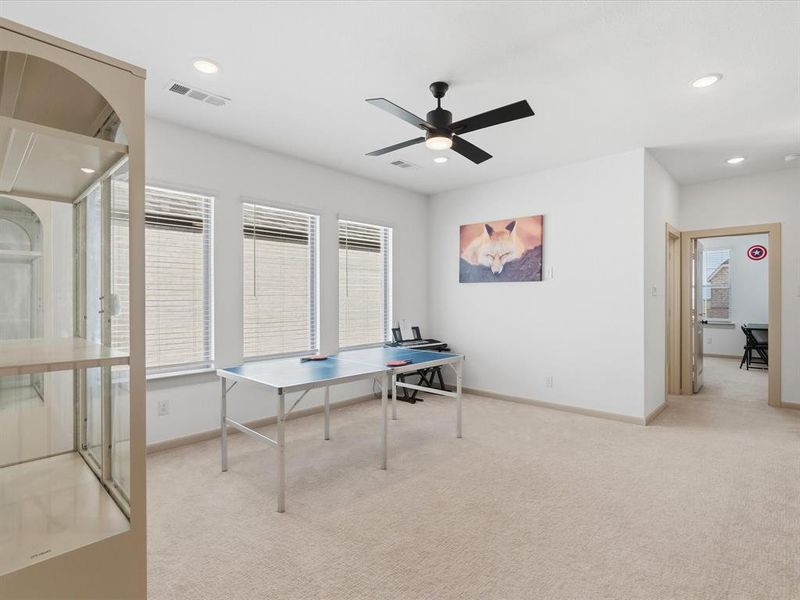 Spacious room featuring neutral carpet flooring, three large windows with blinds, a ceiling fan, and recessed lighting