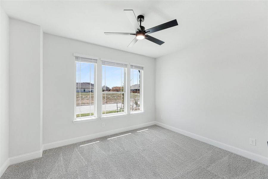 Empty bedroom with gray carpet, ceiling fan, and triple window with neighborhood view