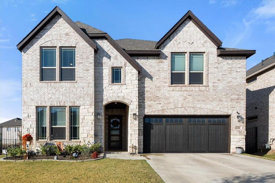French country home with concrete driveway, brick siding, a garage, a front lawn, and stone siding