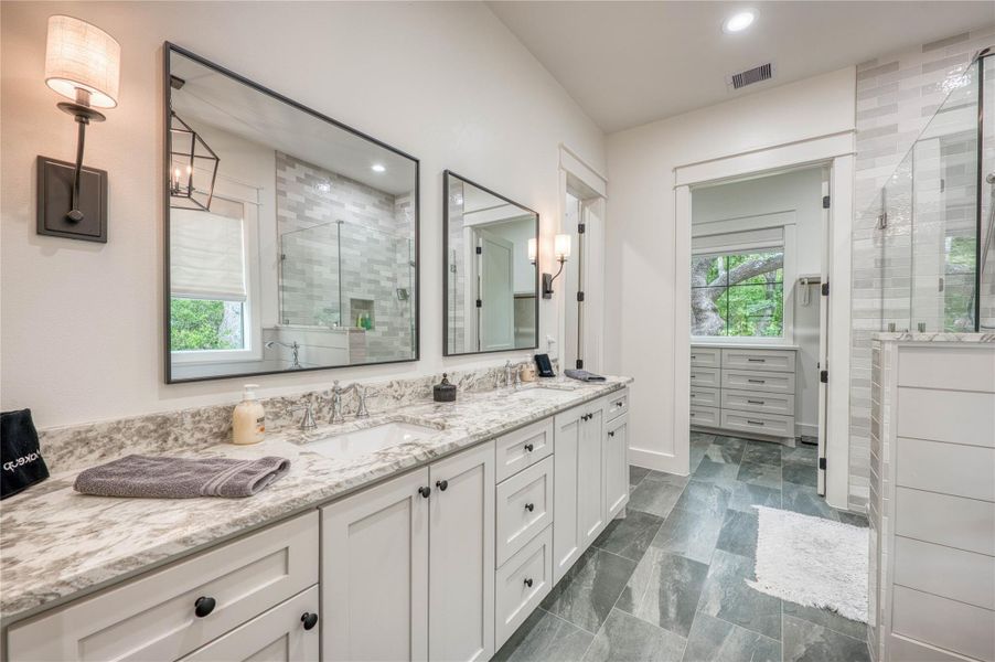 Double vanity with integrated sinks, granite countertops, white cabinetry, and matte black hardware
