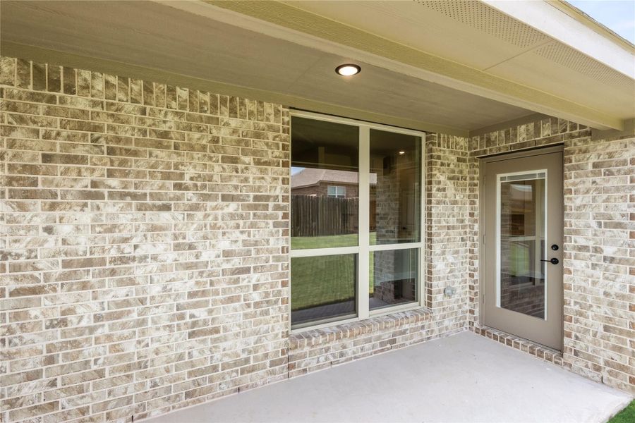 Covered back patio with brick exterior wall, glass door, and large window overlooking backyard Covered back patio with brick exterior wall, glass door, and large window overlooking backyard