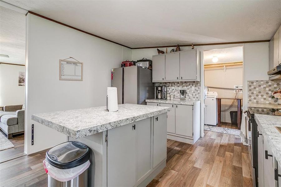 Kitchen with appliances with stainless steel finishes, a kitchen island, decorative backsplash, and light wood-type flooring