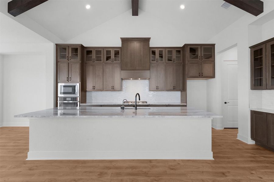Kitchen with beamed ceiling, decorative backsplash, light stone countertops, glass insert cabinets, and appliances with stainless steel finishes