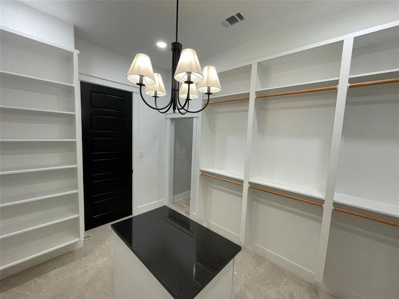 Custom closet system featuring extensive shelving, hanging rods, a central island with a dark countertop, and a five-light chandelier
