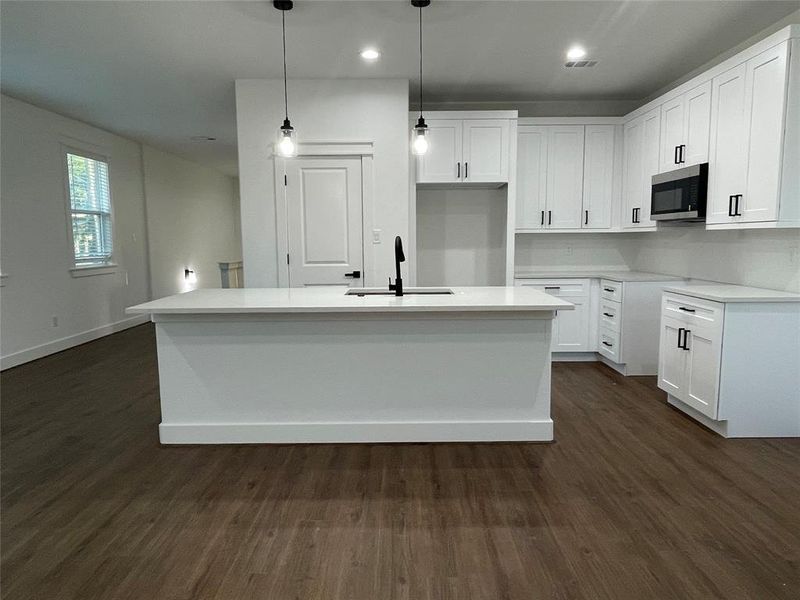 Kitchen with dark wood-style flooring, white cabinetry, light stone counters, hanging light fixtures, and recessed lighting