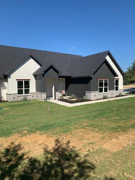 Modern farmhouse style home featuring a shingled roof, a front lawn, board and batten siding, and a porch Modern farmhouse style home featuring a shingled roof, a front lawn, board and batten siding, and a porch