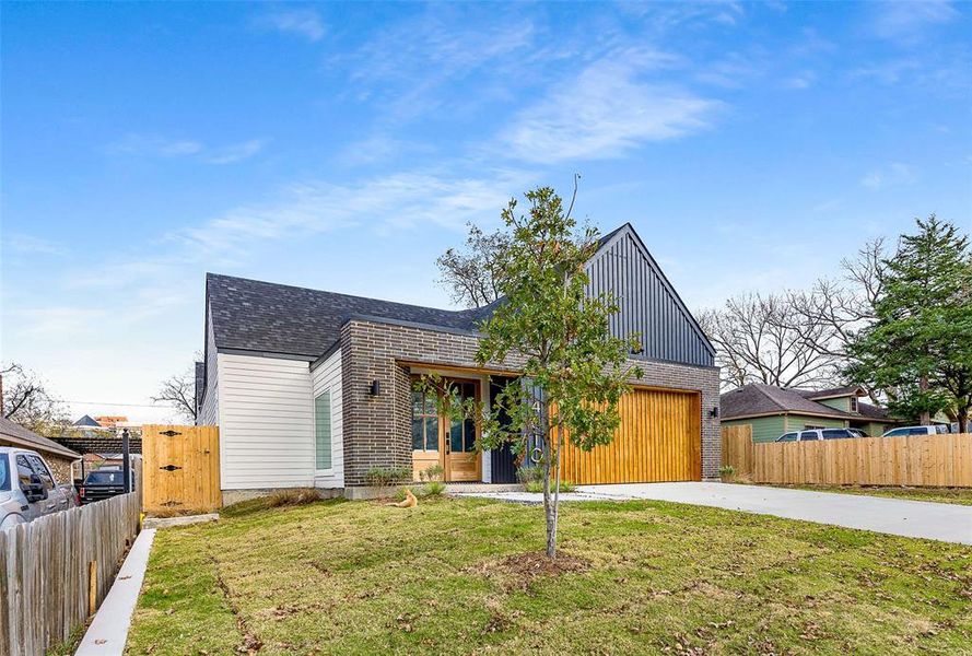 Modern home featuring roof with shingles, driveway, brick siding, and board and batten siding