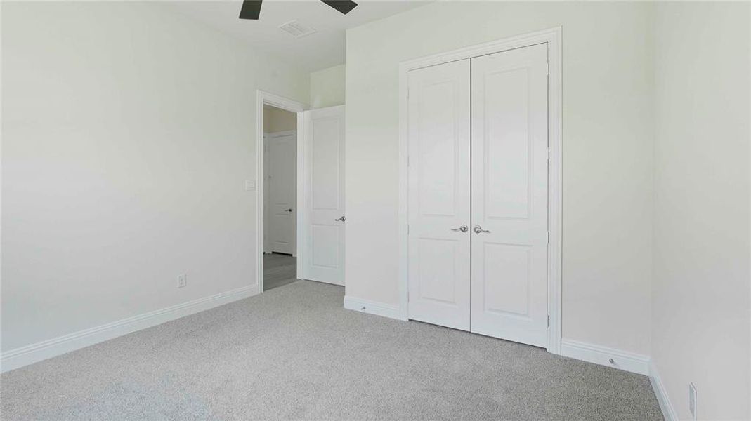 Spacious interior room featuring light-toned carpeting, white baseboards, and a ceiling fan
