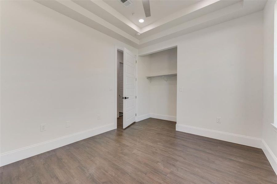 Unfurnished bedroom with a closet, a tray ceiling, dark hardwood / wood-style flooring, and ceiling fan