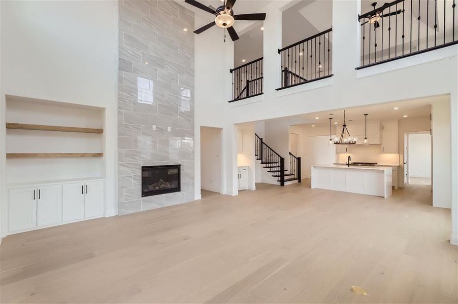 Unfurnished living room with a high ceiling, ceiling fan with notable chandelier, light hardwood / wood-style flooring, and a fireplace