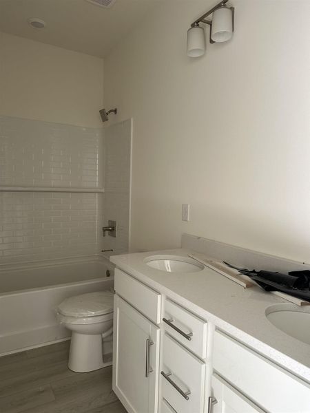Bathroom featuring double vanity, shower / washtub combination, and dark wood-style floors