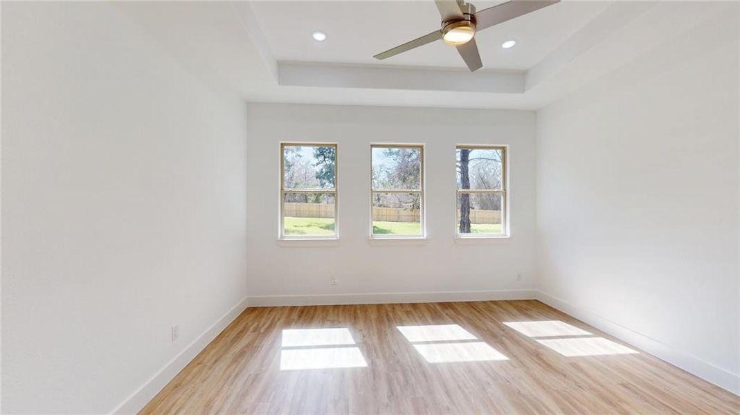 Empty room with light wood-style flooring, baseboards, a raised ceiling, and recessed lighting