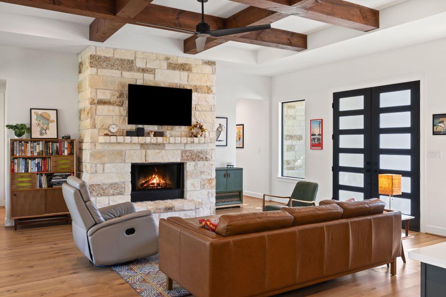 Living room featuring coffered ceiling, light wood-style flooring, a fireplace, beam ceiling, and ceiling fan