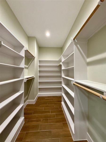 This photo shows a spacious walk-in closet featuring multiple shelves and hanging rods, with wood-look tile flooring and recessed lighting for a bright, organized space.