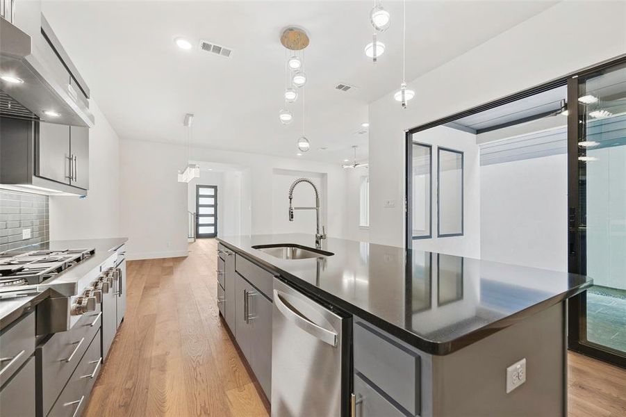 Kitchen featuring under cabinet range hood, gray cabinetry, stainless steel appliances, a sink, and visible vents