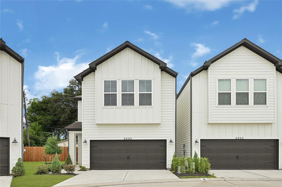 This photo shows a modern two-story house with a clean white exterior and contrasting dark garage doors. It features a small front yard with minimal landscaping and a driveway. The house is part of a row of similar homes, suggesting a suburban neighborhood setting. This photo shows a modern two-story house with a clean white exterior and contrasting dark garage doors. It features a small front yard with minimal landscaping and a driveway. The house is part of a row of similar homes, suggesting a suburban neighborhood setting.