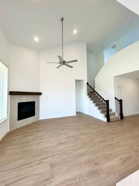 Spacious room featuring vaulted ceilings, wood-finish flooring, a contemporary fireplace with a tiled surround and wood mantel, and a staircase with dark wood newel posts and metal balusters Spacious room featuring vaulted ceilings, wood-finish flooring, a contemporary fireplace with a tiled surround and wood mantel, and a staircase with dark wood newel posts and metal balusters