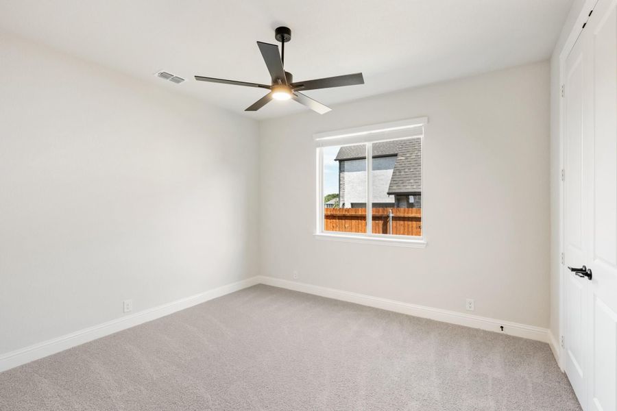 Empty bedroom with gray carpet, ceiling fan, and a window overlooking a wood fence