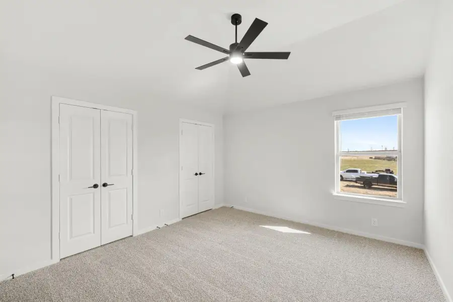 Empty bedroom with carpet, black ceiling fan, two closets, and a window with outdoor views