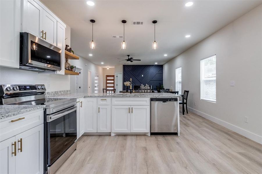 Kitchen featuring ceiling fan, white cabinets, light wood-type flooring, light stone countertops, and appliances with stainless steel finishes