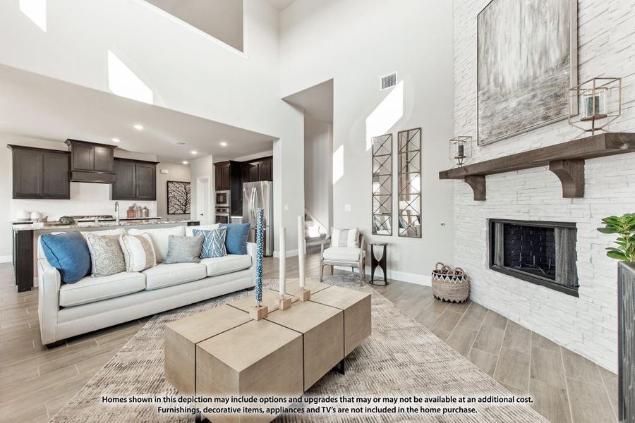 Open living room with two-story ceiling, stone fireplace, and open view to kitchen with dark cabinets Open living room with two-story ceiling, stone fireplace, and open view to kitchen with dark cabinets