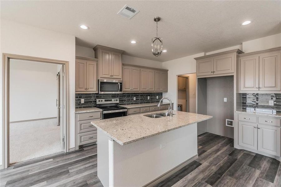 Kitchen with stainless steel appliances, light stone countertops, decorative backsplash, an island with sink, and dark wood-style floors