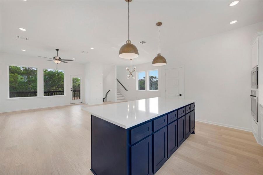 Spacious open-concept kitchen and living area featuring a large island with white countertop, recessed lighting, and light wood-finish flooring