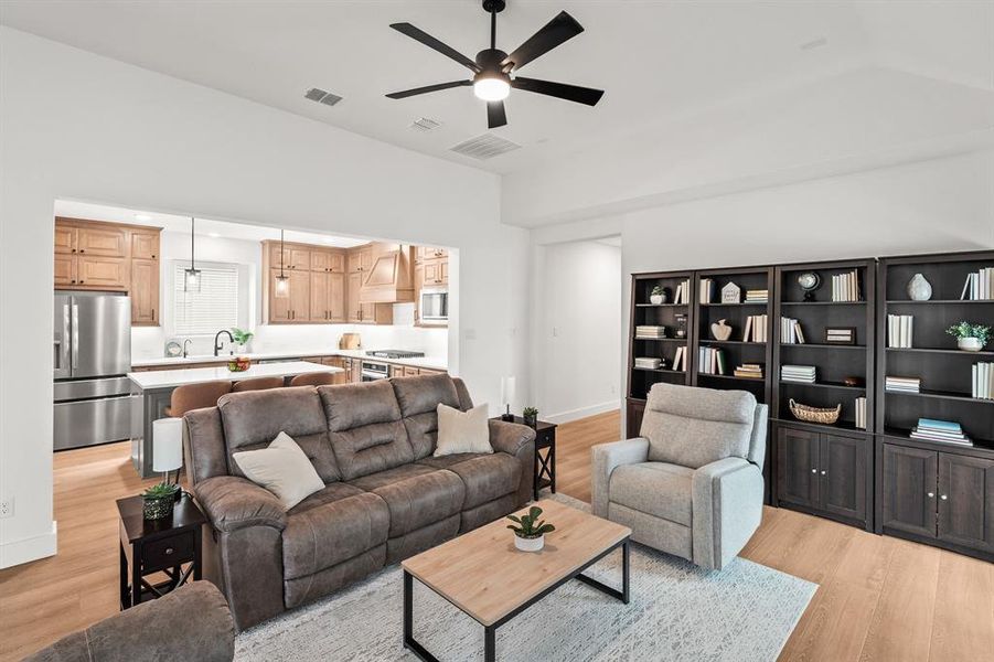 Living room with light wood-style floors, a ceiling fan, and vaulted ceiling Living room with light wood-style floors, a ceiling fan, and vaulted ceiling