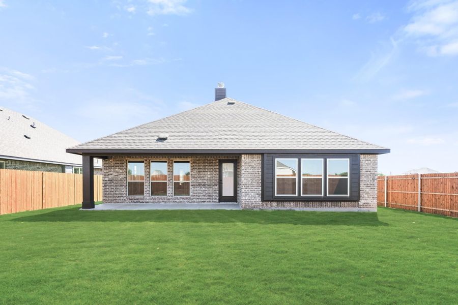 Rear exterior of single-story brick home with covered patio, large windows, and fenced backyard with green lawn. Rear exterior of single-story brick home with covered patio, large windows, and fenced backyard with green lawn.