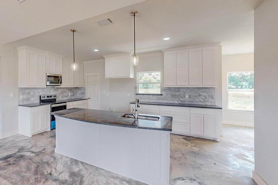 Kitchen featuring appliances with stainless steel finishes, backsplash, sink, a center island with sink, and white cabinets