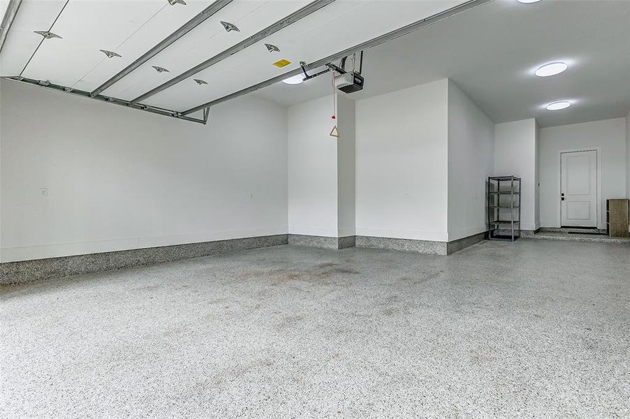 Spacious and clean three-car garage with a sleek epoxy floor, ample lighting, and a convenient entry door, perfect for storage or parking.