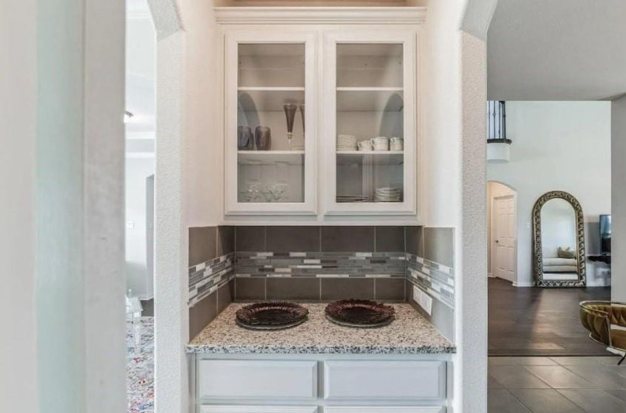 Bar featuring dark wood-type flooring, light stone countertops, decorative backsplash, and white cabinetry