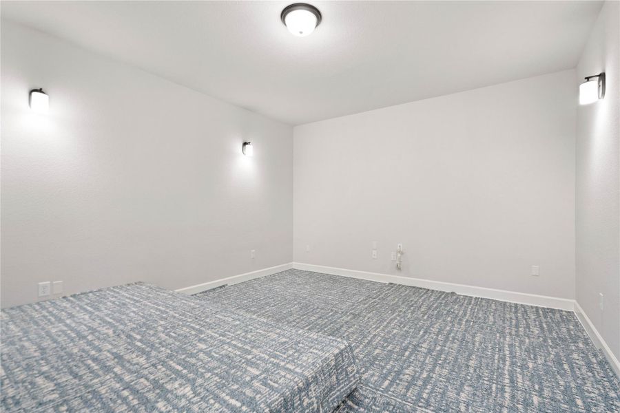 Patterned carpet anchors a flexible bonus room flanked by modern wall sconces.