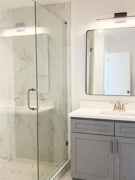 Glass-enclosed shower featuring white marble-look wall tiles and a light-toned mosaic floor
