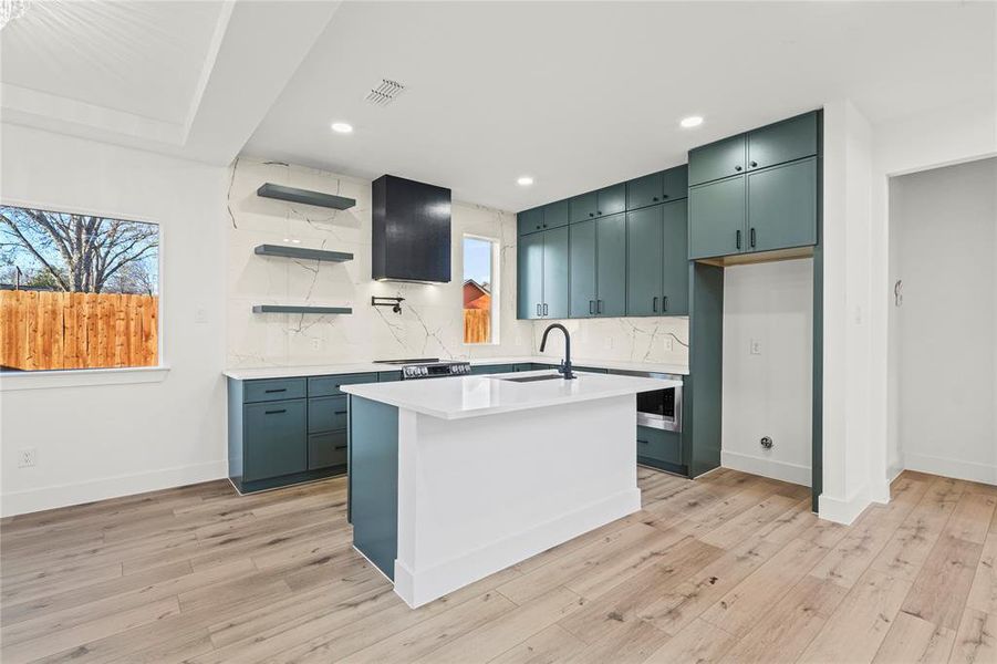 Kitchen featuring a center island with sink, open shelves, plenty of natural light, decorative backsplash, and recessed lighting