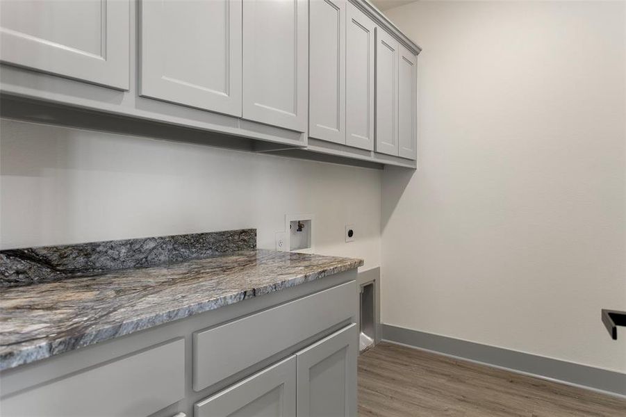 Clothes washing area with hookup for a washing machine, cabinets, light wood-type flooring, and hookup for an electric dryer