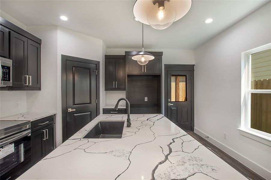 Kitchen with pendant lighting, hardwood / wood-style floors, light stone countertops, range, and sink