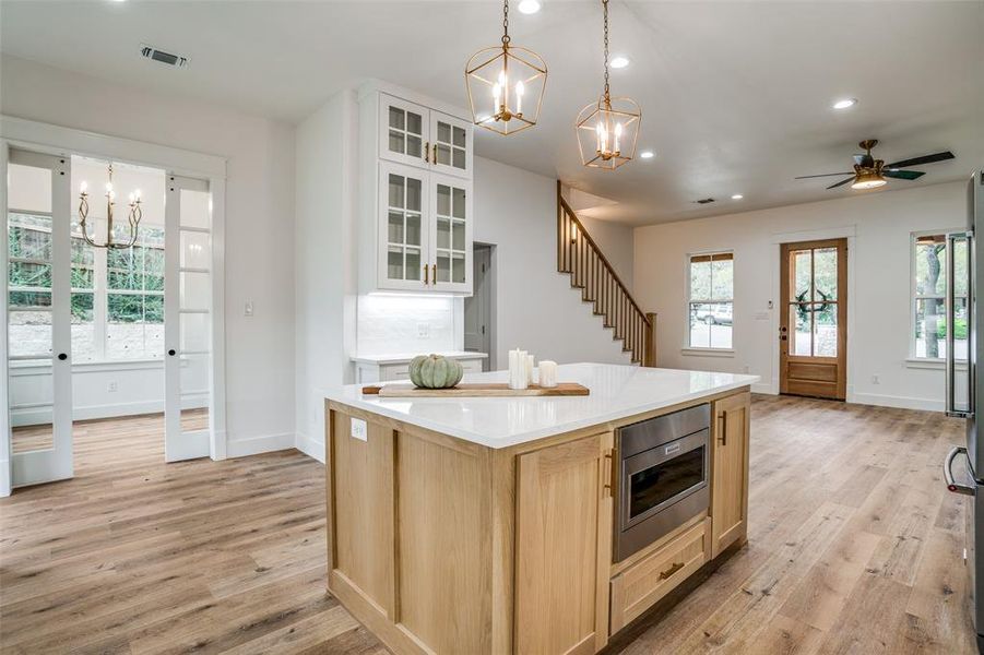 Kitchen featuring light brown cabinetry, stainless steel microwave, a center island, and light wood-type flooring