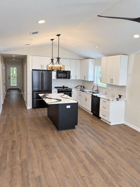 Vaulted ceiling with recessed lighting, wood-finish flooring, white cabinetry, a black kitchen island with a light-toned countertop, and black appliances Vaulted ceiling with recessed lighting, wood-finish flooring, white cabinetry, a black kitchen island with a light-toned countertop, and black appliances