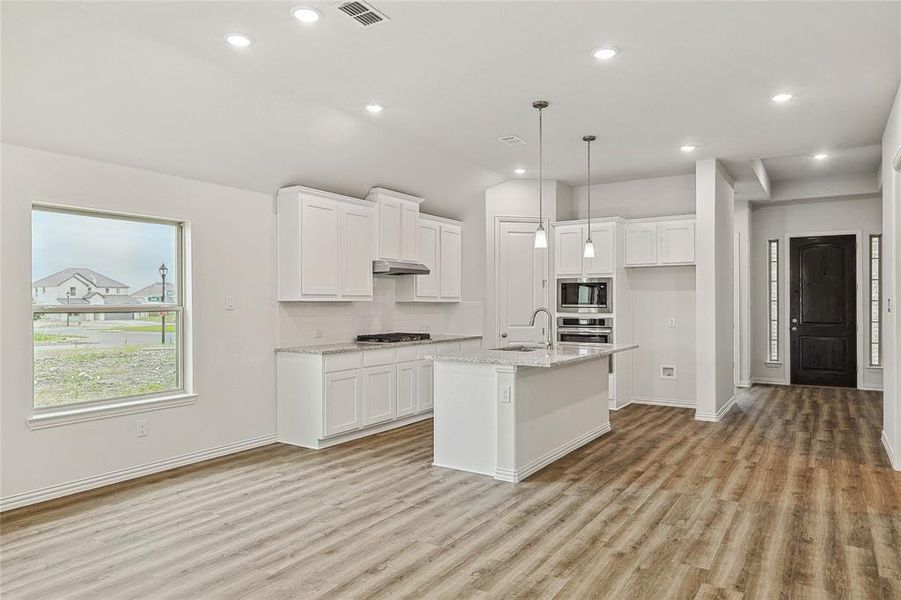 Kitchen featuring appliances with stainless steel finishes, light hardwood / wood-style floors, white cabinetry, and an island with sink