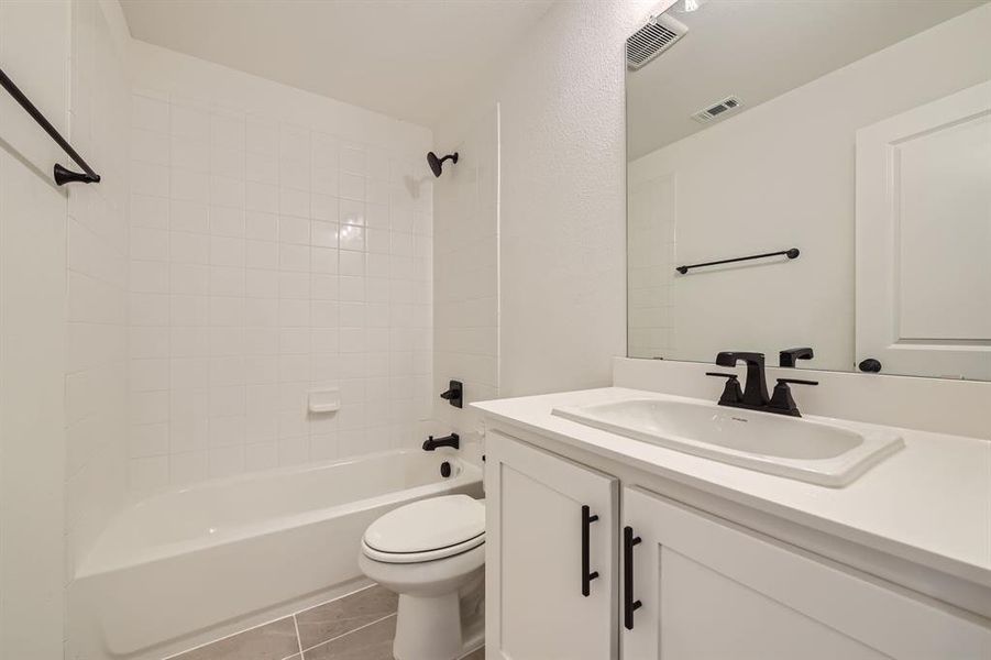 Full bathroom featuring vanity, toilet, tile patterned floors, and tiled shower / bath combo