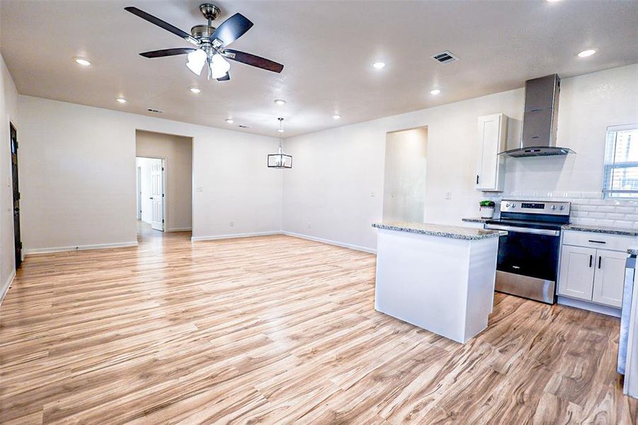 Kitchen with stainless steel range with electric stovetop, wall chimney range hood, ceiling fan, light wood-style flooring, and light stone counters